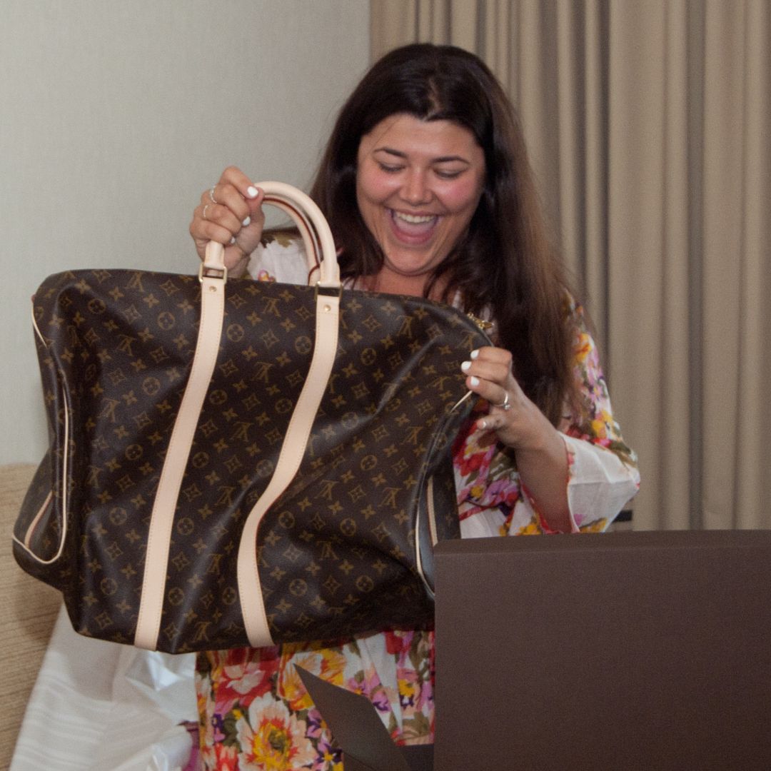 brunette woman smiling as she opens a Louis Vuitton bag as a gift
