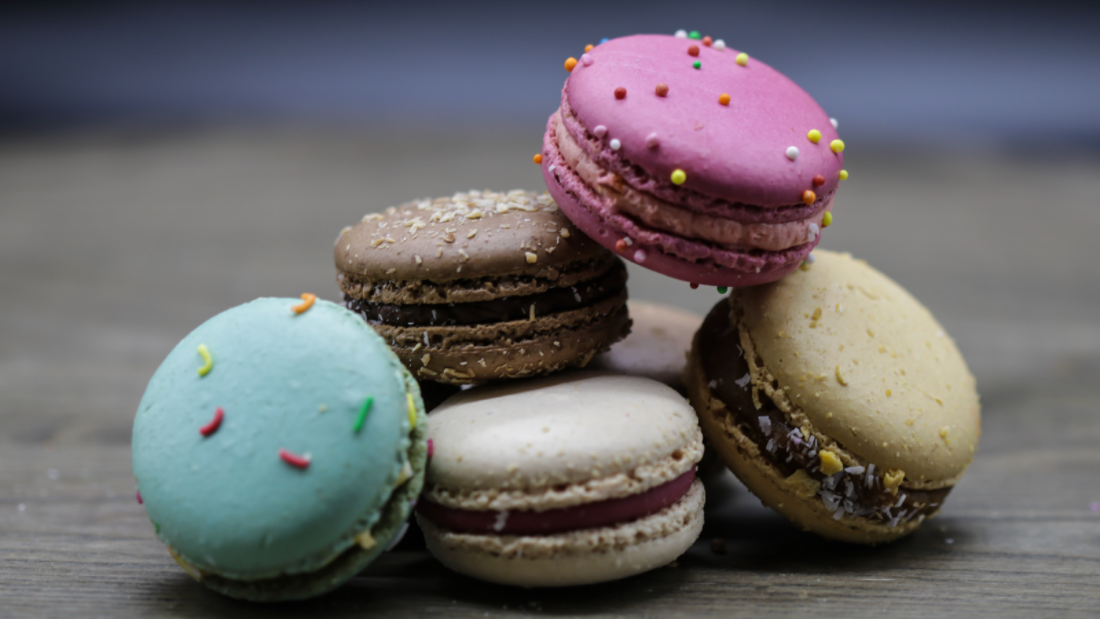 5 colorful macaroons arranged arranged together. They are blue, brown, beige, pink, and green.