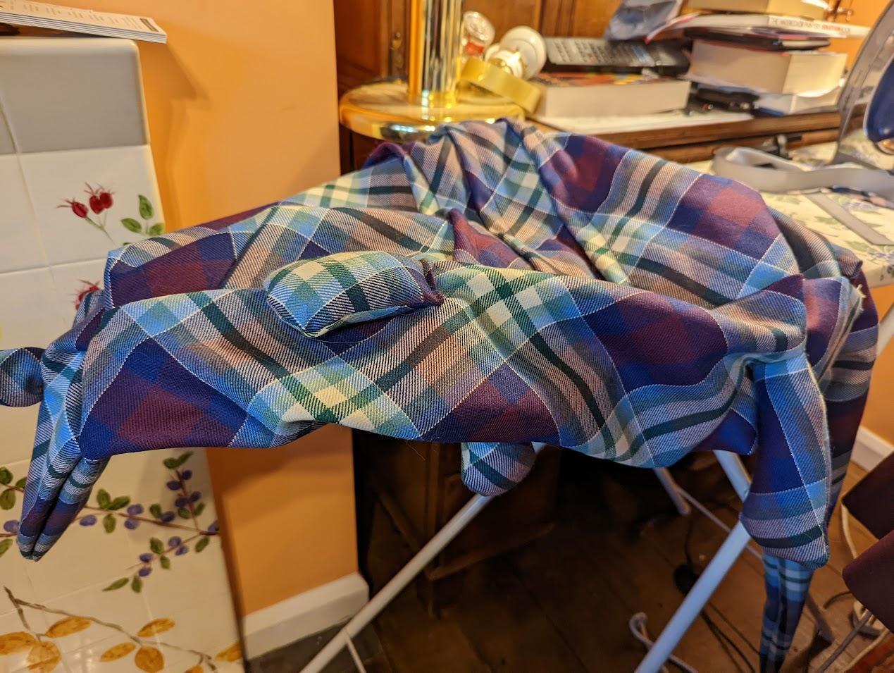 The unstuffed form of the tartan armadillo fabric toy sits on top of an ironing board. 