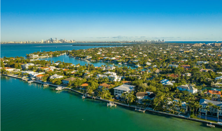 Aerial view of Key Biscayne in Miami, Florida. Homes are built right up to the water with private docks and a view of downtown Miami in the background.