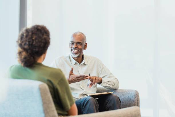 Unrecognizable woman listens as cheerful counselor gestures and speaks An unrecognizable mid adult woman listens as the cheerful mature adult male counselor gestures and speaks. adult counseling stock pictures, royalty-free photos & images
