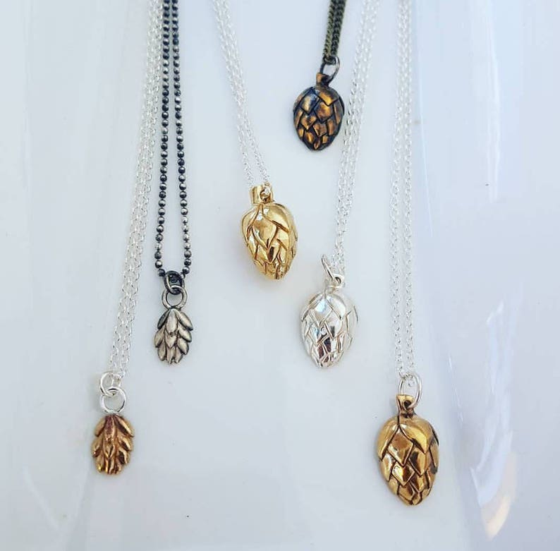 A photo of six necklaces featuring hop cone pendants of various sizes, in gold, copper, brass and silver. 