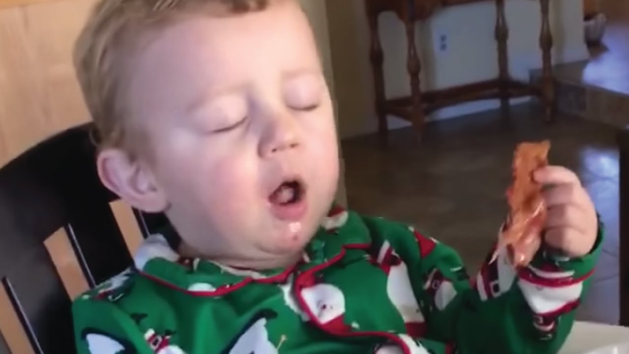 Child holding a piece of bacon with his eyes closed.