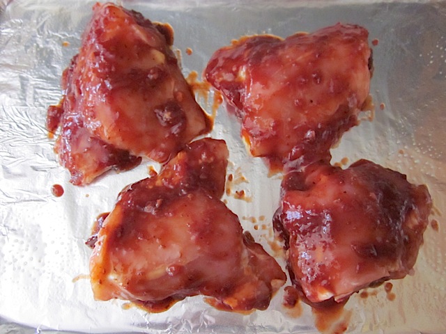 chicken placed on baking sheet covered in aluminum foil and then covered in bbq sauce