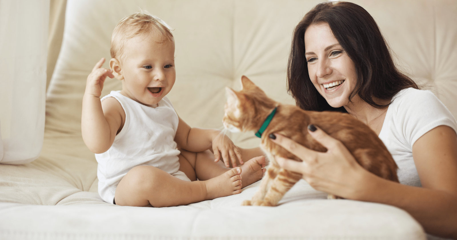 Baby sitting on couch smiling at mom holding kitten