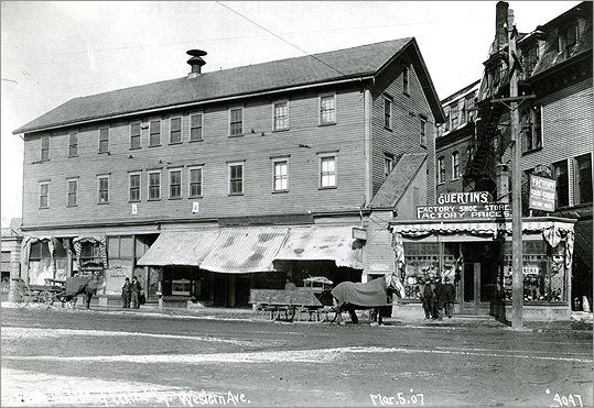Street level view of three story wooden building. First floor has awnings over windows. Horses, carts, and several people are in front of building. Handwritten on bottom of image "Western Ave/March 5, 07/4047"