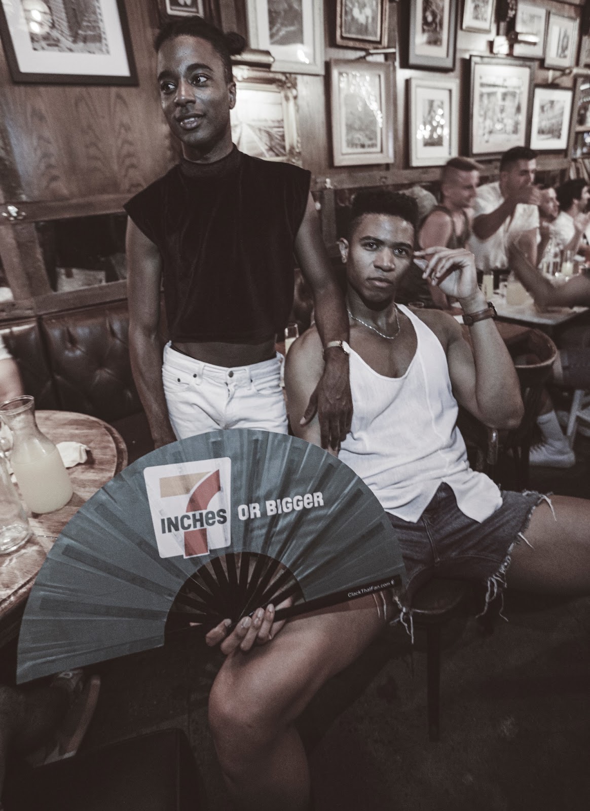 Men at a bar, one holds a fan that reads 