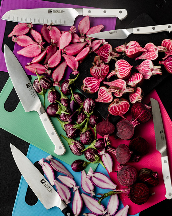 Zwilling knives laid over colorful cutting boards, surrounded by pink and purple cut produce