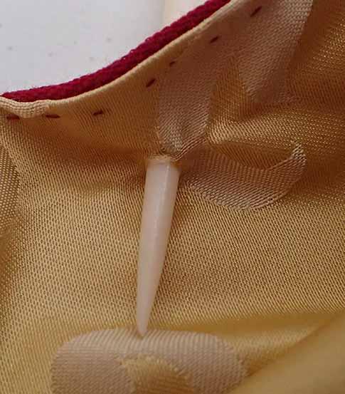 A close up shot of the bone awl that has pierced through both layers of fabric, with the point visible from the cream silk edge.