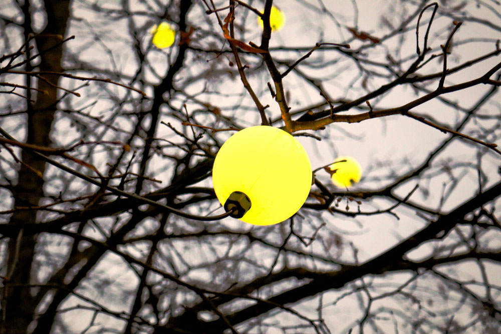 Spherical yellow lamp bulb hanging on a tree branch on the leafless tree and sepia evening sky background