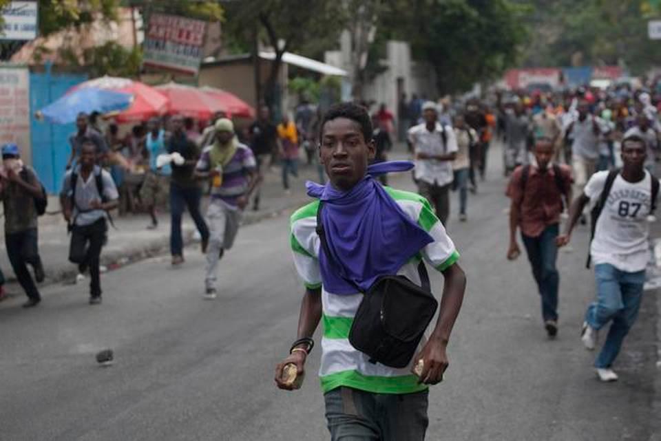 Protesters run while holding stones during a protest demanding that the government lower fuel prices, in Port-au-Prince, Haiti, Friday, Feb. 13, 2015. Students marched through Haiti's capital to demand lower gas prices and the ouster of President Michel Martelly.