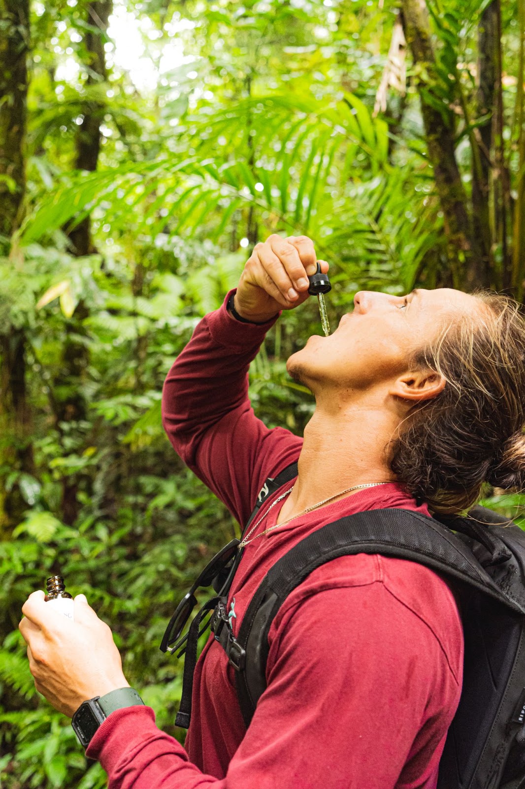 Young man taking CBD tincture sublingually (under the tongue) in the jungle of costa rica