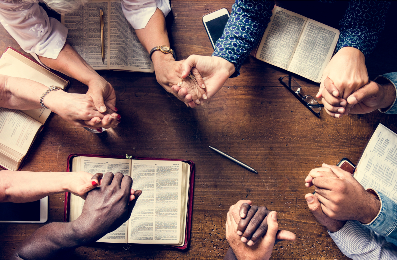 a group of people sharing in worship by holding hands in a circle over some bibles