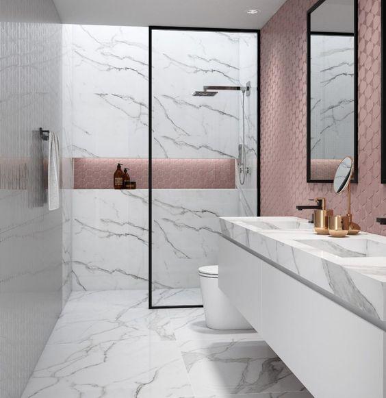 Banheiro com revestimento marmorizado branco nas paredes, piso e bancada da pia, armário branco, box de vidro e espelhos com molduras pretas, parede da pia e faixa do banheiro com revestimento hexagonal rosa.