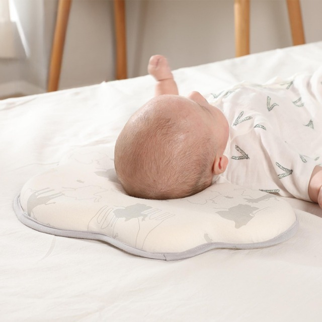 bebelus care sta intins pe spate cu capul pe o perna anti-plagiocefalie