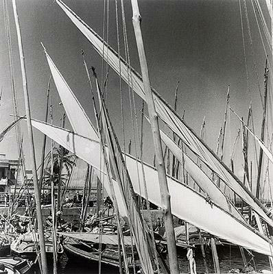 Reprodução fotográfica do artista. Um porto de barcos. Alguns barcos espalhados pela imagem, o foco está nas velas. 