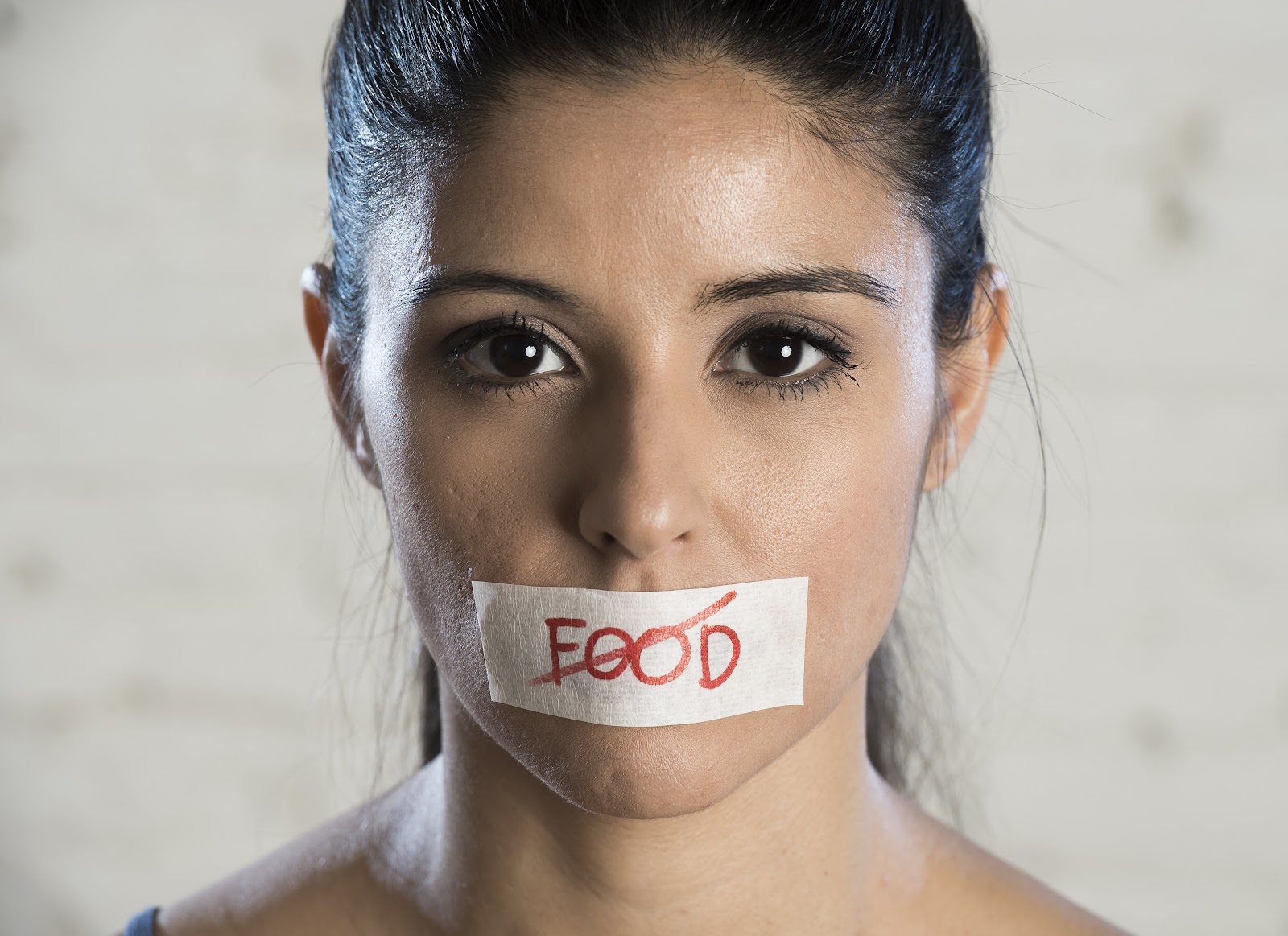 A woman with tape that says food crossed out over her mouth 