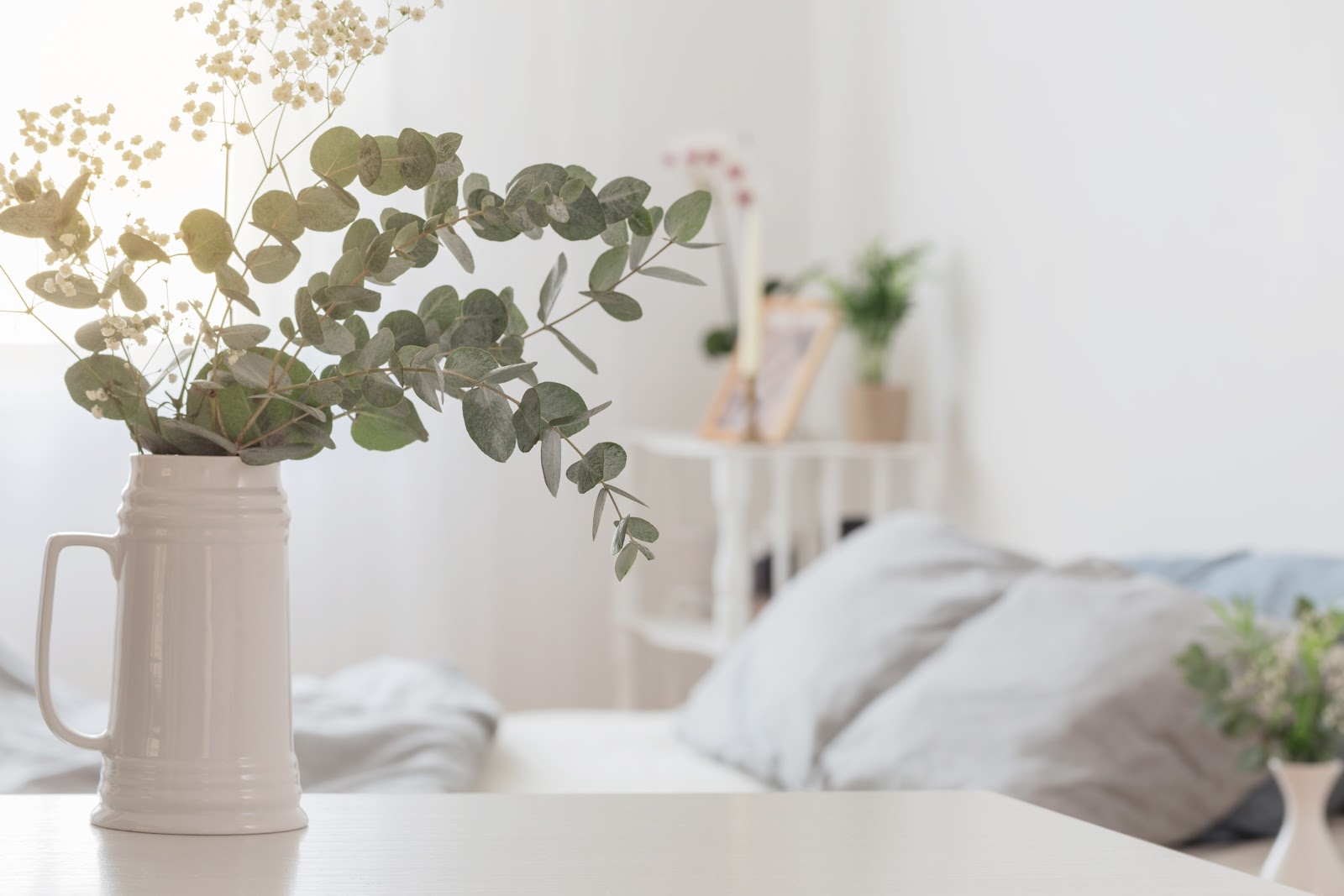 Eucalyptus and gypsophila flowers in a jug in white bedroom.