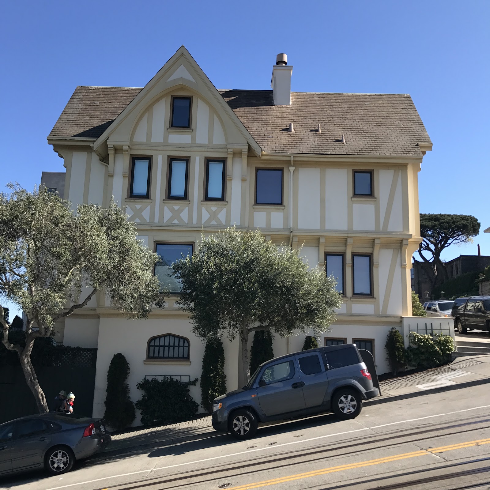 san francisco yellow 3 story home on a crooked street with two cars in the front and iconic tram route