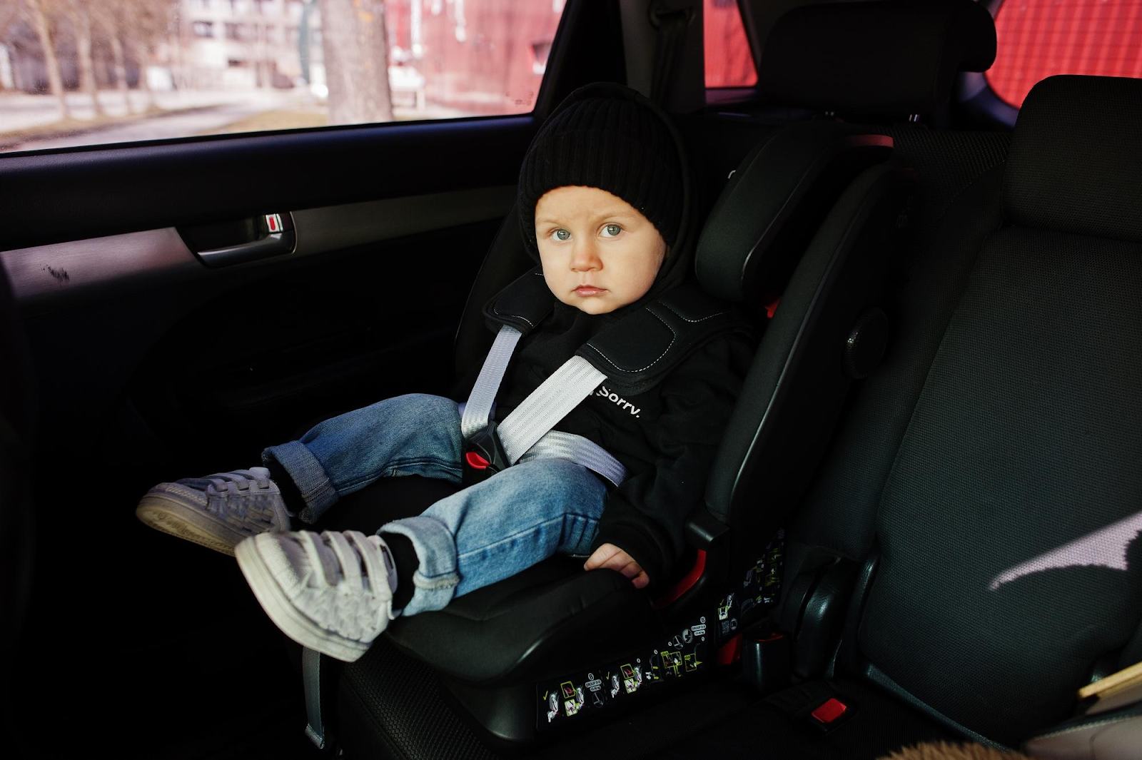 chlapček v čiernom svetríku, modrých nohaviciach a čiernej čiapke pripútaný v čiernej autosedačke