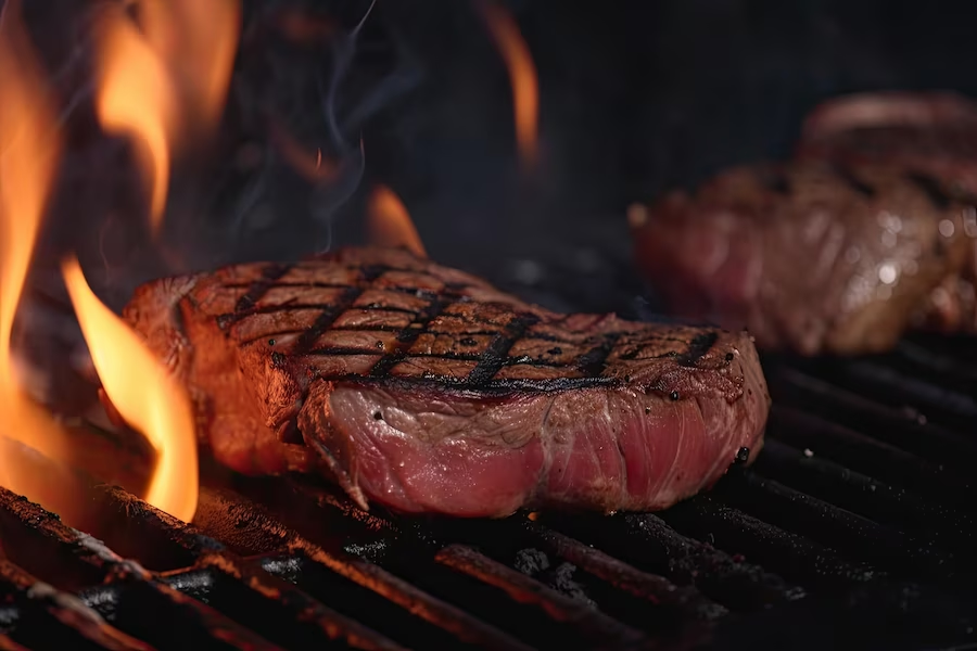 Grilled beef steaks on a BBQ grill, cooking over a fire