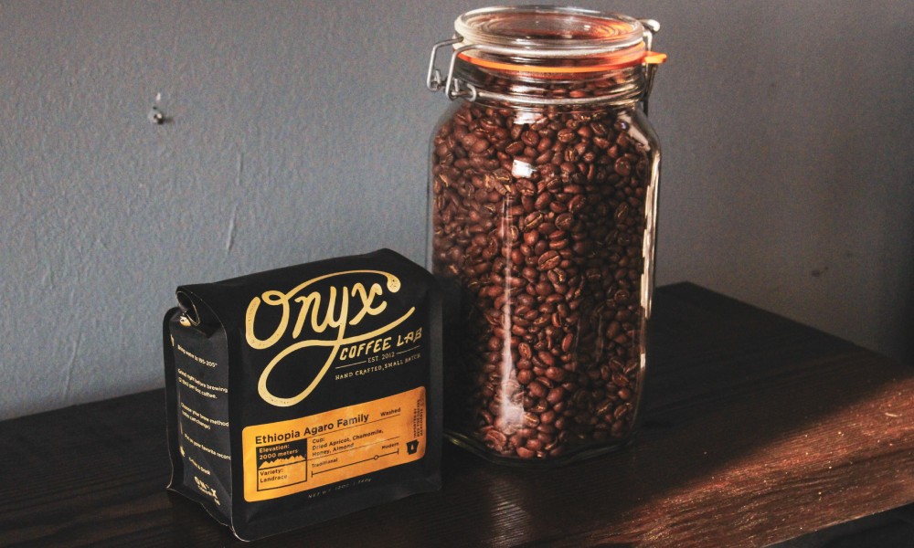 Black and gold Onyx Coffe Lab coffee pouch beside glass mason jar filled with dark roasted coffee beans. 