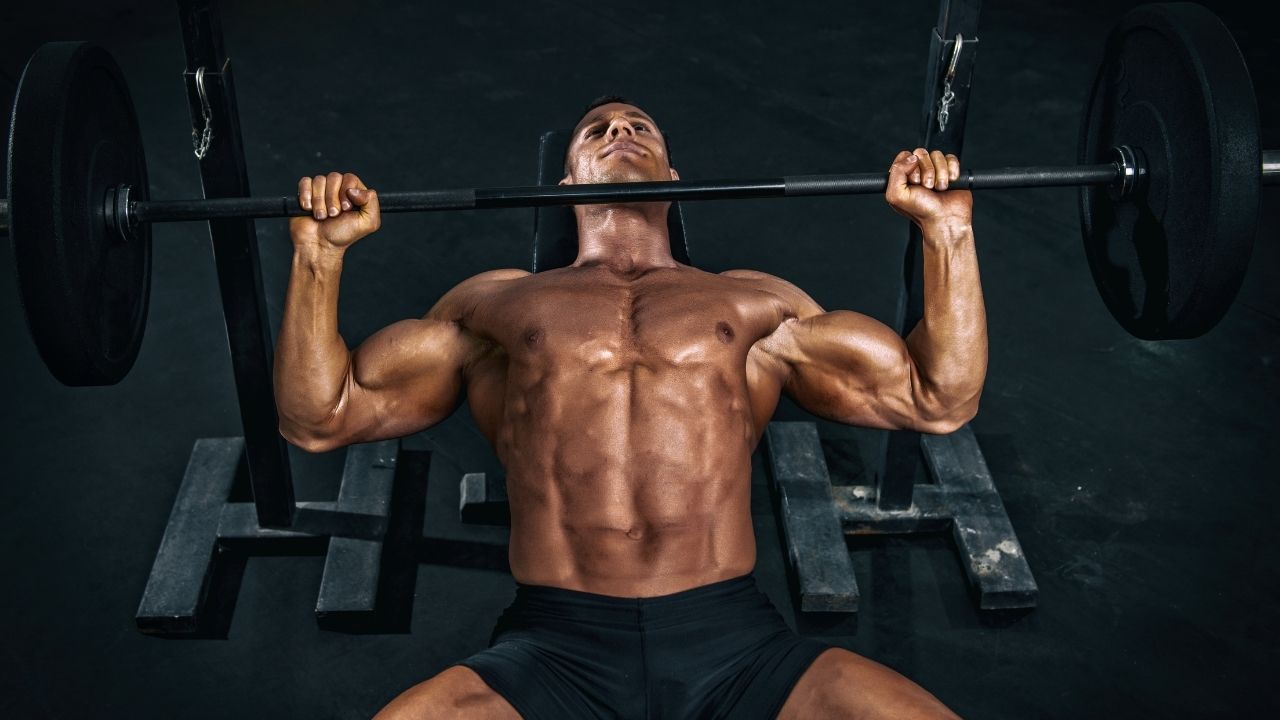 A man performs barbell bench press exercise in the gym.