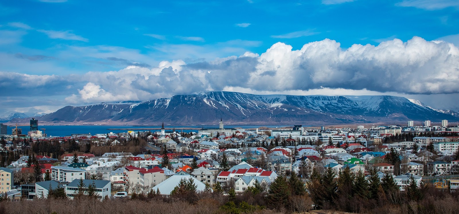 reykjavik iceland calm town skyline panoramic view from distance with large mountain and water in background on a sunny day