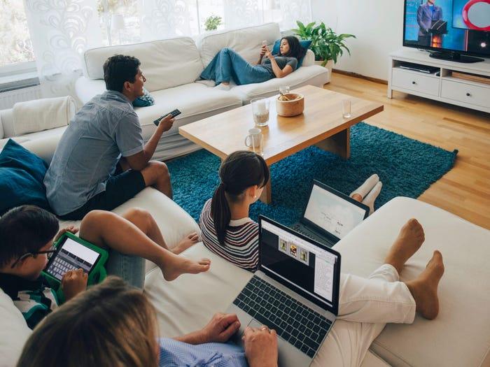 family watching tv at home with laptops and tablets