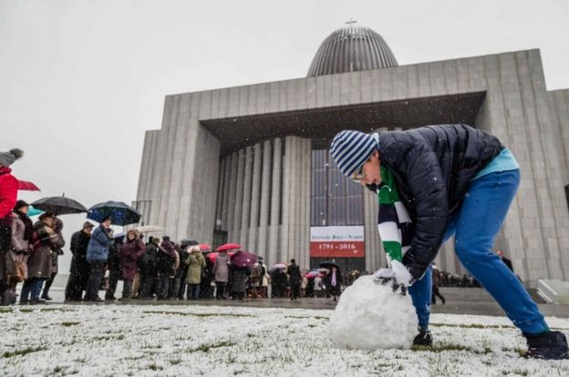 A young man makes a snowball as people queue to enter the Temple of Divine Providence before the opening ceremonies, on November 11, 2016.