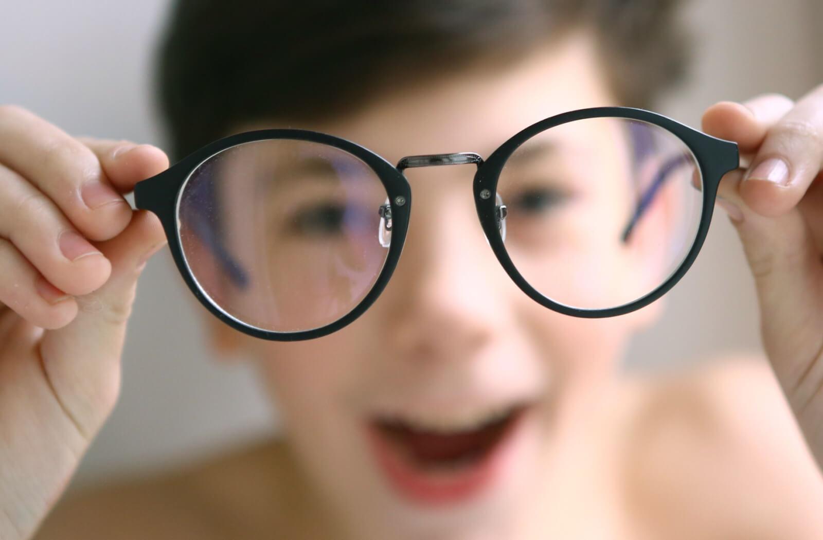 a child with myopia holds his glasses close to the camera. the image is blurry, except for through the lenses of the glasses