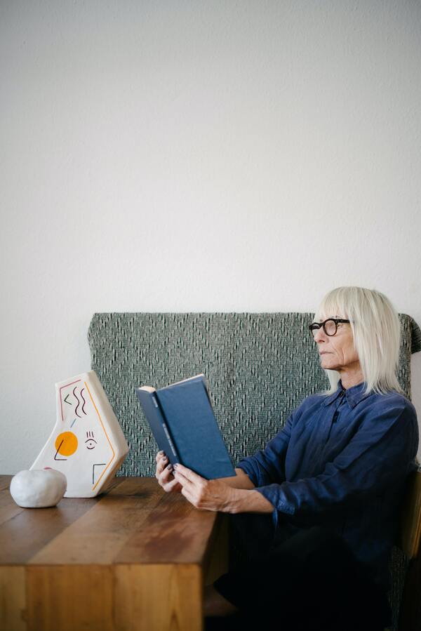 Foto de uma senhora sentada lendo um livro. 