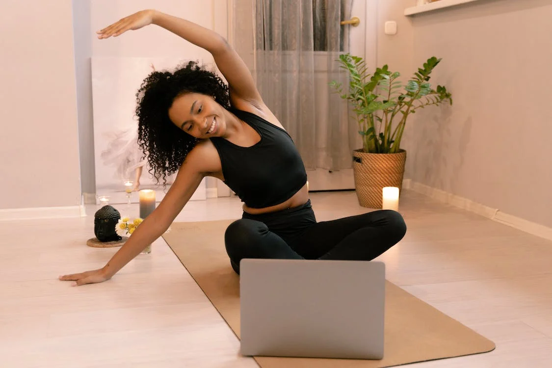 Woman with Curly Hair Doing Stretching on a Yoga Mat with a Laptop