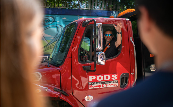A driver for PODS City Service is waving from the red cab of his truck as he’s preparing to park and ready a PODS container for unloading in Chicago. 
