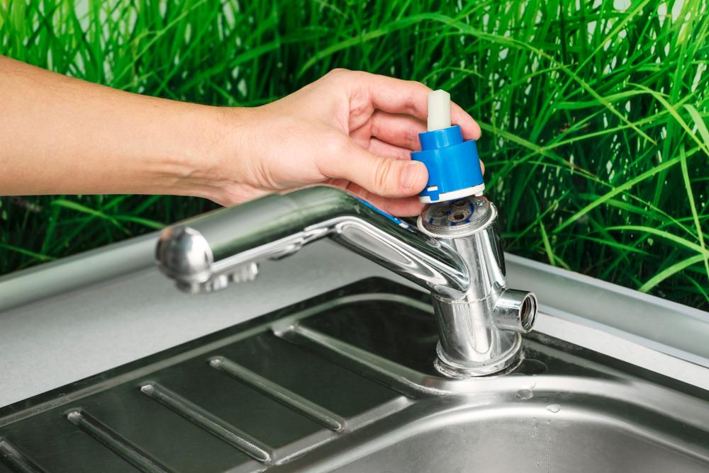 Hand removing cartridge from kitchen sink with grass in the background