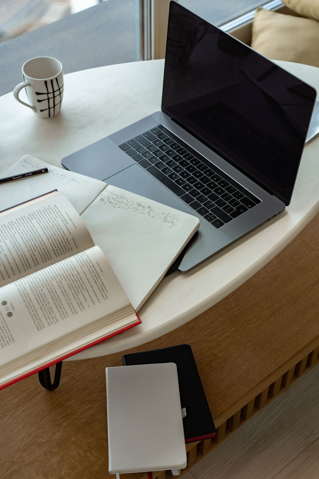 Image of open book, notebooks and laptop on coffee table