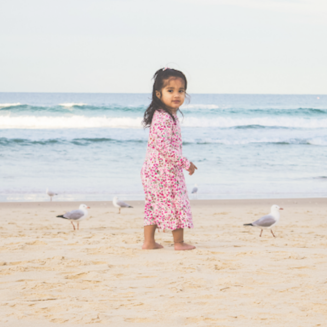 A little girl in a flowery dress on a beach surrounded by birds