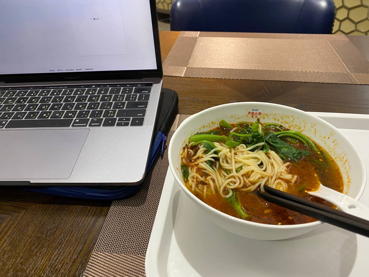 Alt text: A bowl of chow mein and a computer on the table of the lounge.