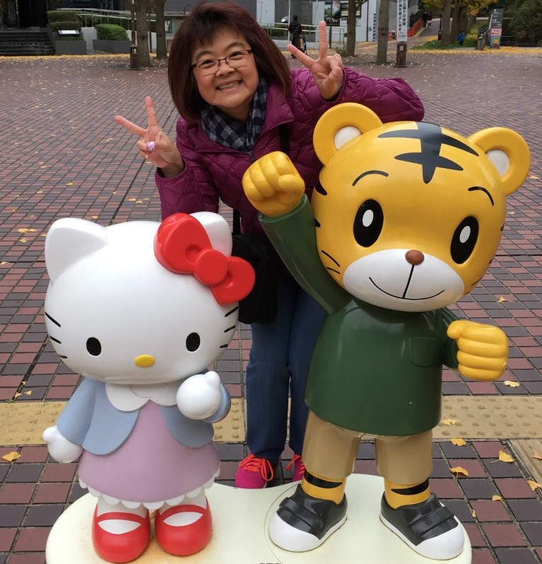 Kim de pelo corto y negro y gafas está de pie junto a las estatuas de Hello Kitty