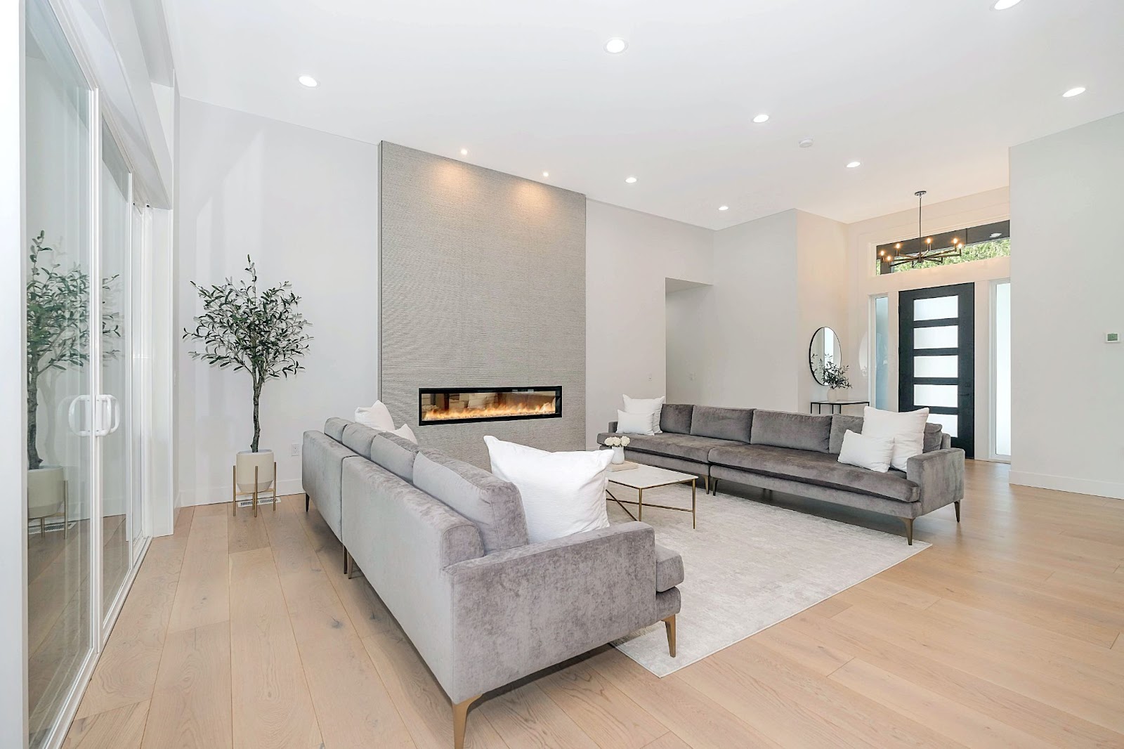 Modern living room in luxury home with white walls, light wood flooring and grey velvet sofas.