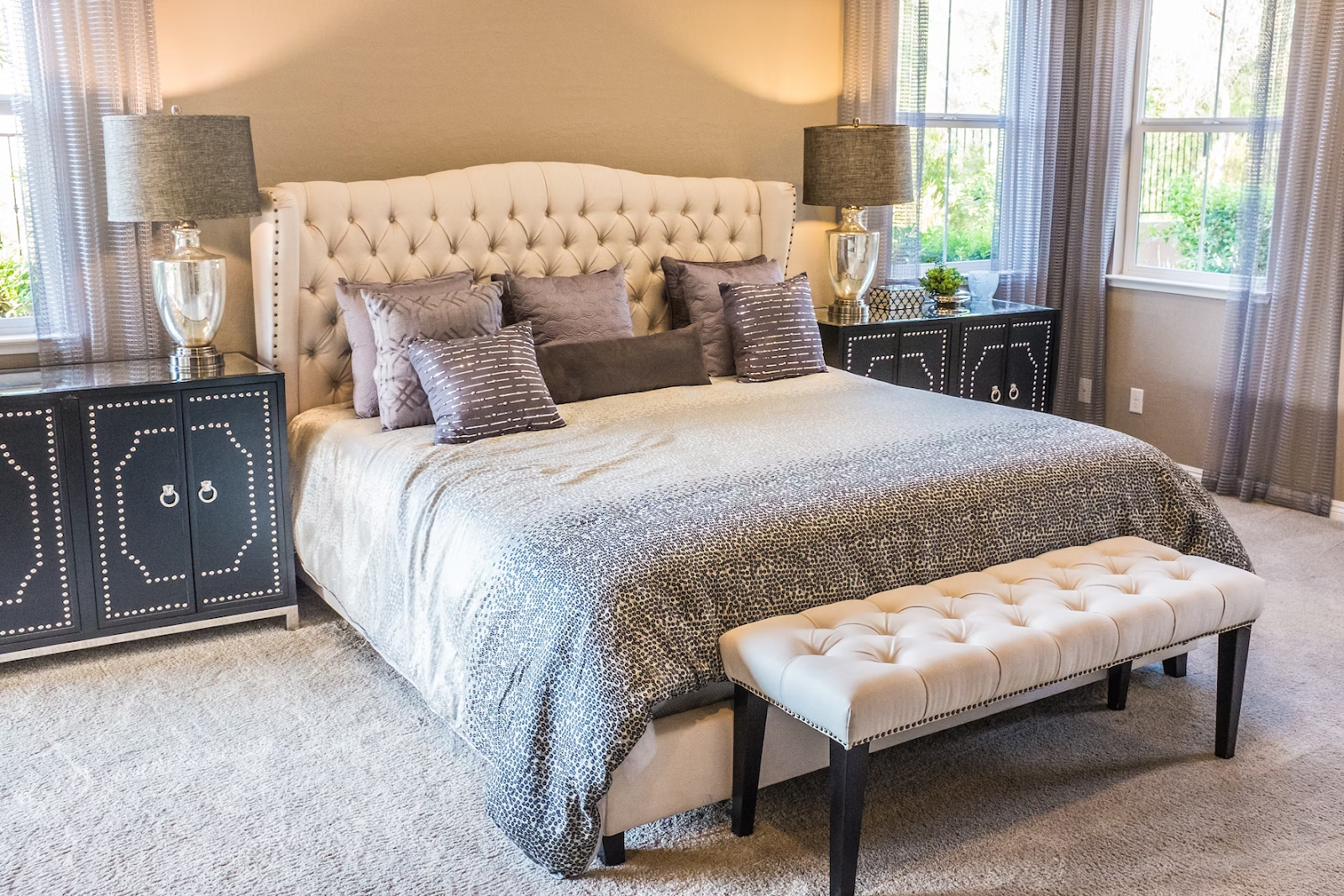 king sized divan bed with cream headboard, silver bed linens and purple scatter cushions in a modern decorated bedroom with black side tables and silver lamps