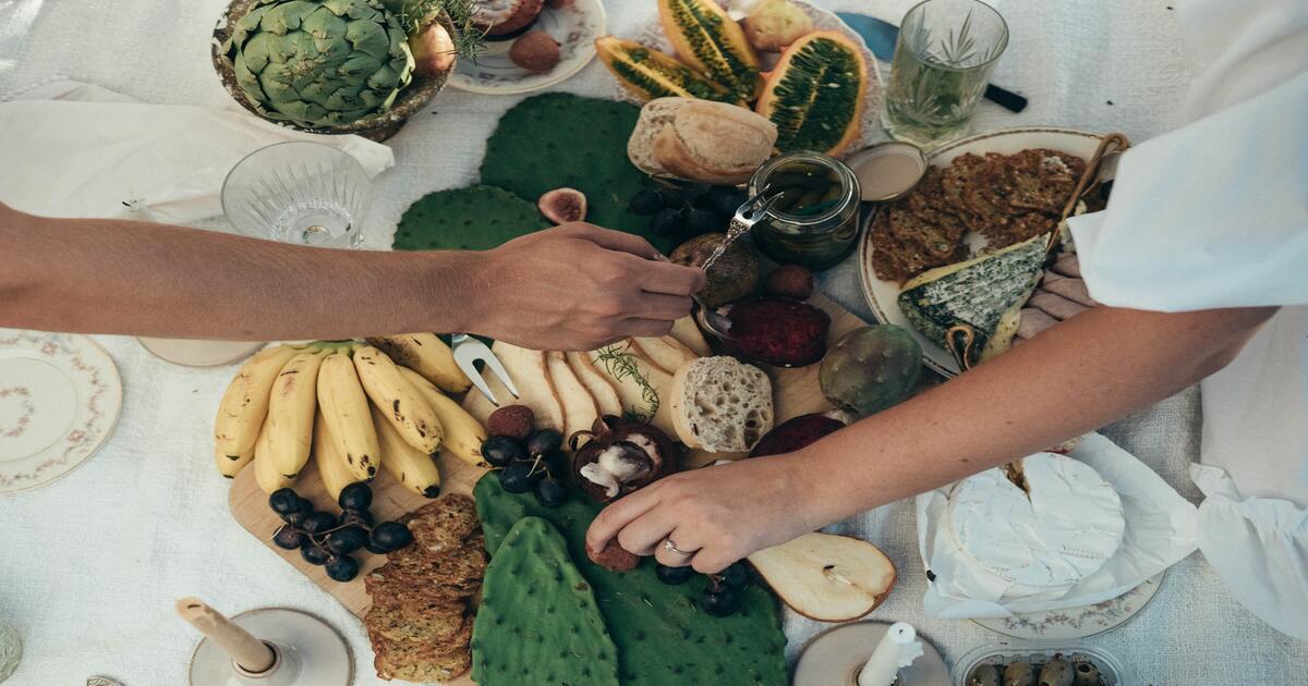 Small business holiday gift guide–A birds eye view image of a table covered in different types of food with hands reaching overtop to grab things. 