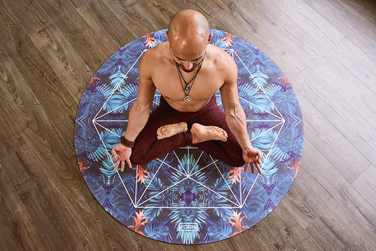Homem sentado em tapete redondo em posição de meditação visto de cima