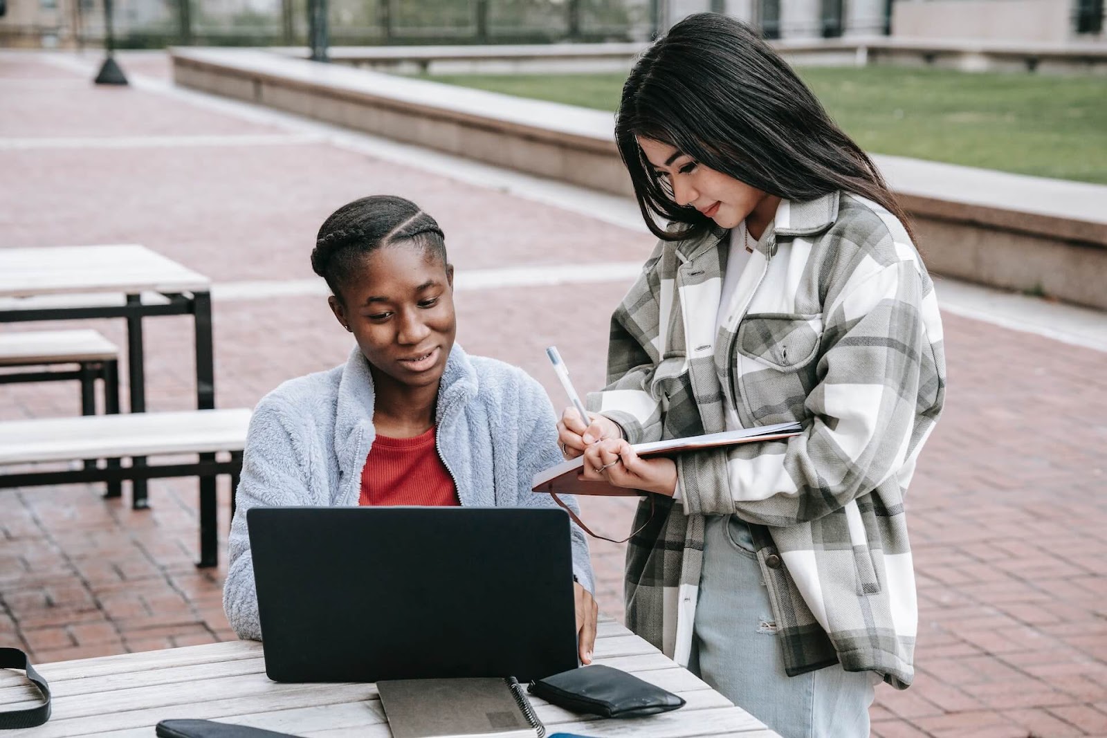 Two students taking notes on a laptop outside