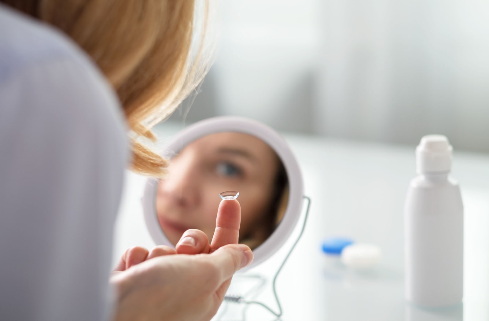 A young woman looking into a small mirror to put in her contact lens.