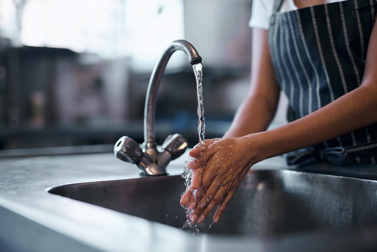 Woman washing her hands with a kitchen sink configuration of a faucet on the right side of the sink