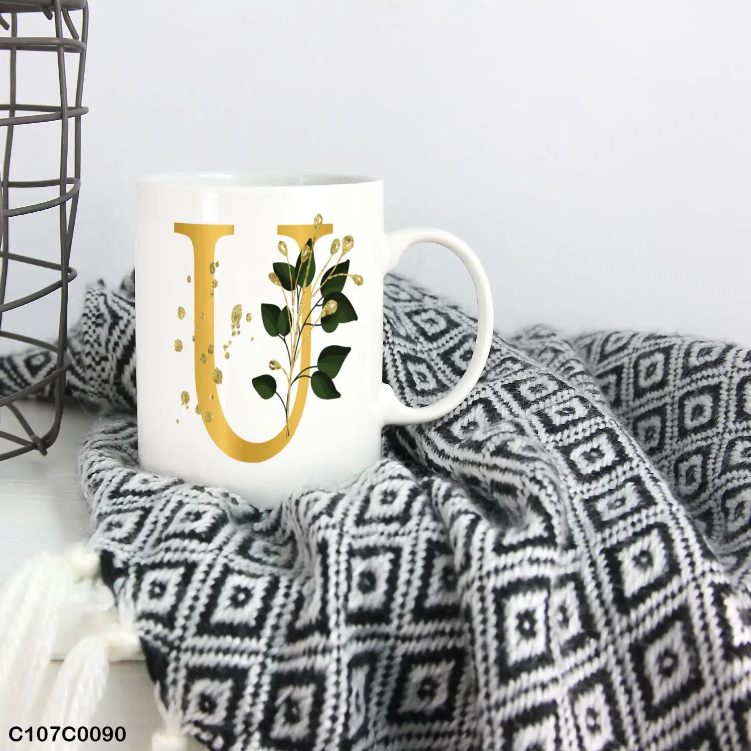 A white mug (cup) printed with gold Letter "U"and small green branch