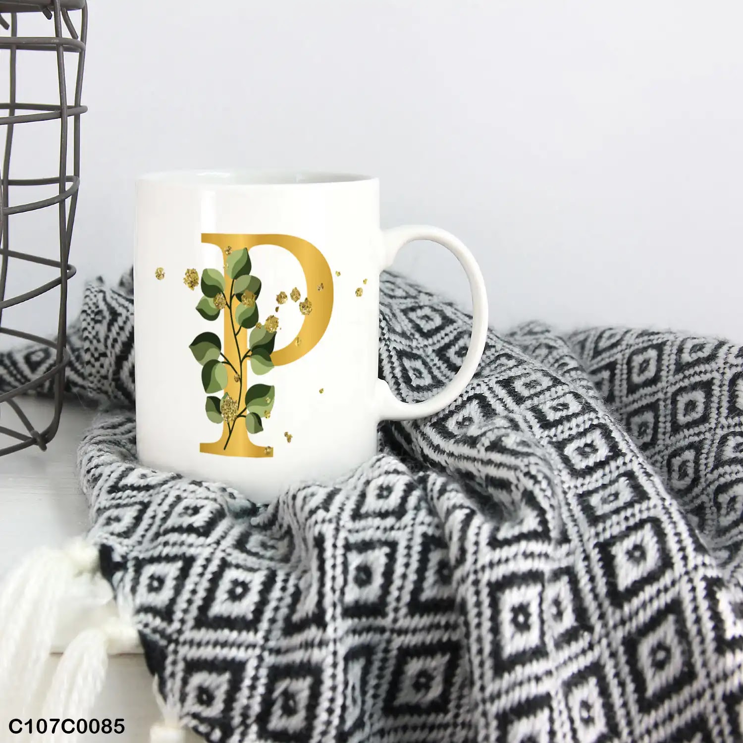 A white mug (cup) printed with gold Letter "P" and small green branch