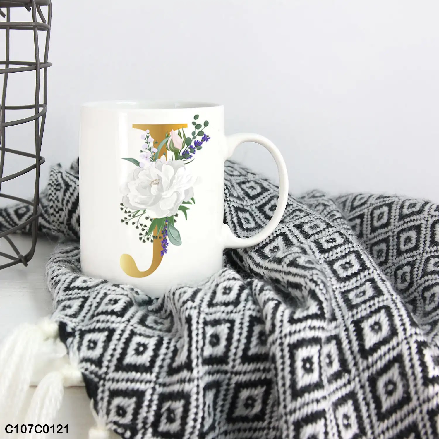 A white mug (cup) printed with gold Letter "J" and small white branch