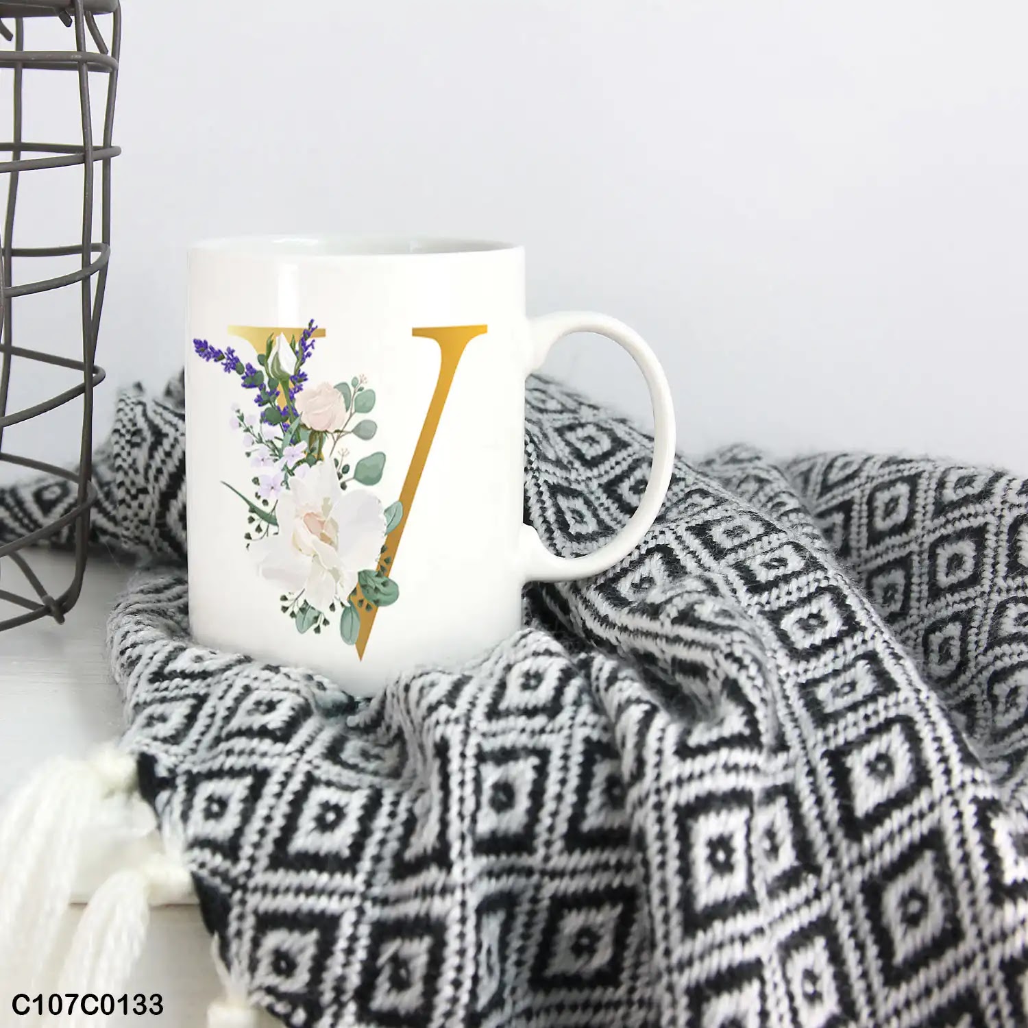 A white mug (cup) printed with gold Letter "V" and small white branch